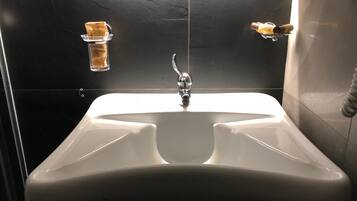 A modern bathroom with a white sink, a chrome faucet, and a soap dispenser on the wall.
