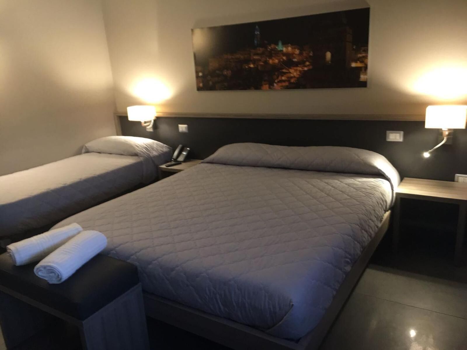 A hotel room with two beds, a nightstand with a lamp, and a painting on the wall.