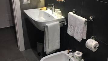 Ein modernes Badezimmer mit einem weißen Waschbecken, einem Bidet, einer Toilette und einem Spiegel.