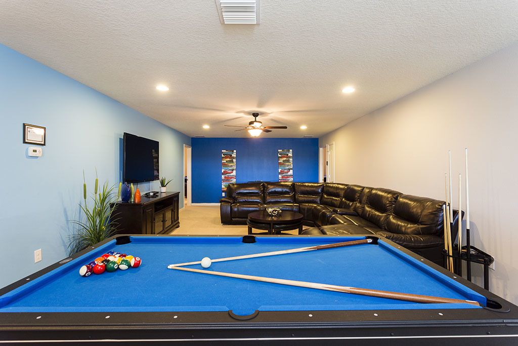 A pool table with balls, a leather couch, and a television in a room with blue walls and a ceiling fan.