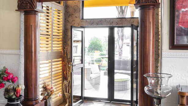 A lobby with a wooden archway, a glass door leading outside, and a marble floor. - SelaMod Village guest House (Chaneng)