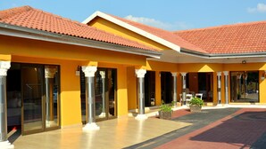 A hotel with a yellow facade, red-tiled roof, and columns with white capitals. - SelaMod Village guest House (Chaneng)