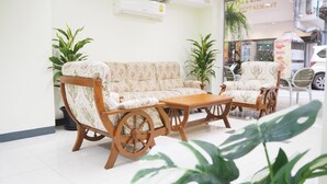 Uma área de recepção com sofá, cadeiras, mesa de centro de madeira e plantas em vasos.