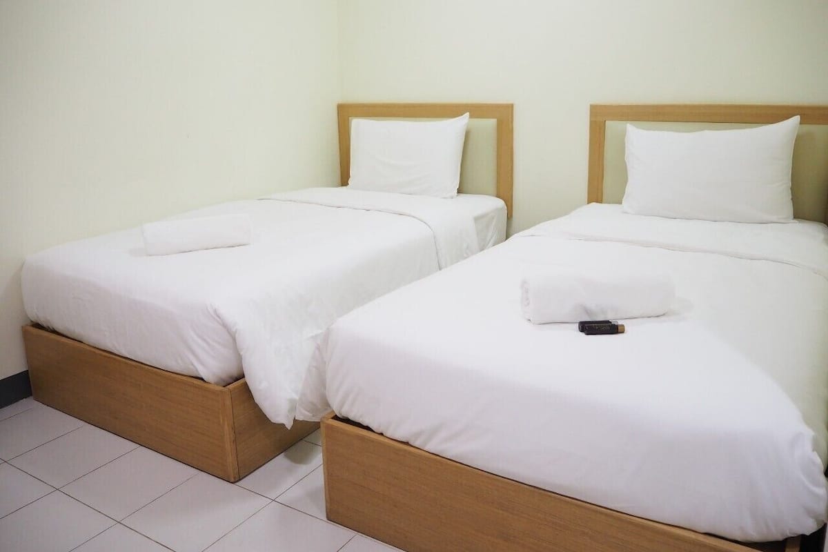 Two single beds with wooden headboards and white bedding in a room with white walls and tiled flooring.