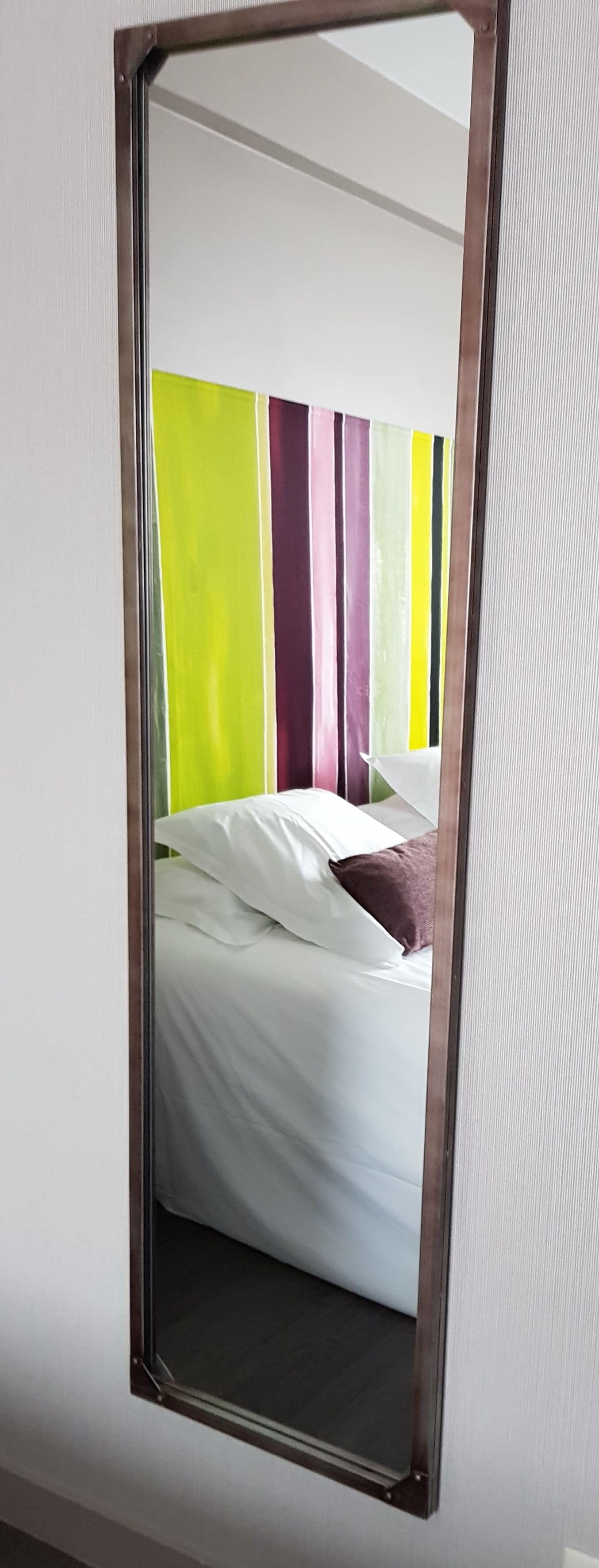 Una habitación con cama, ropa de cama blanca y un cabecero a rayas coloridas.