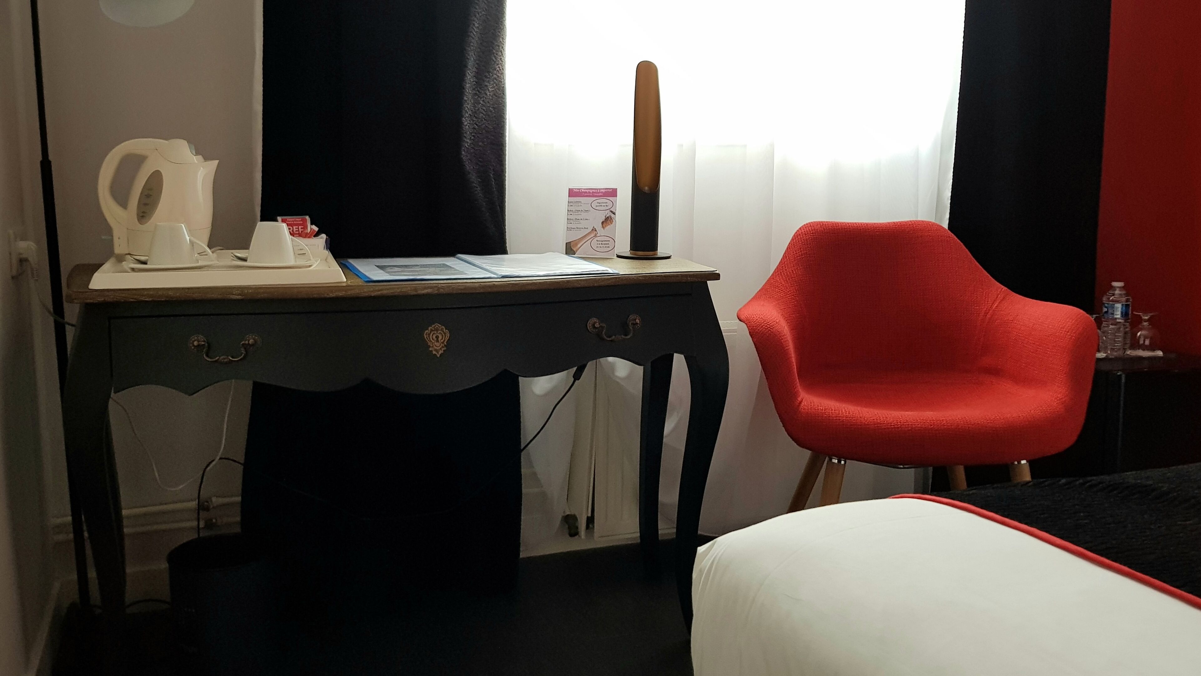 A room with a desk, a red chair, a bed, and a window with curtains.