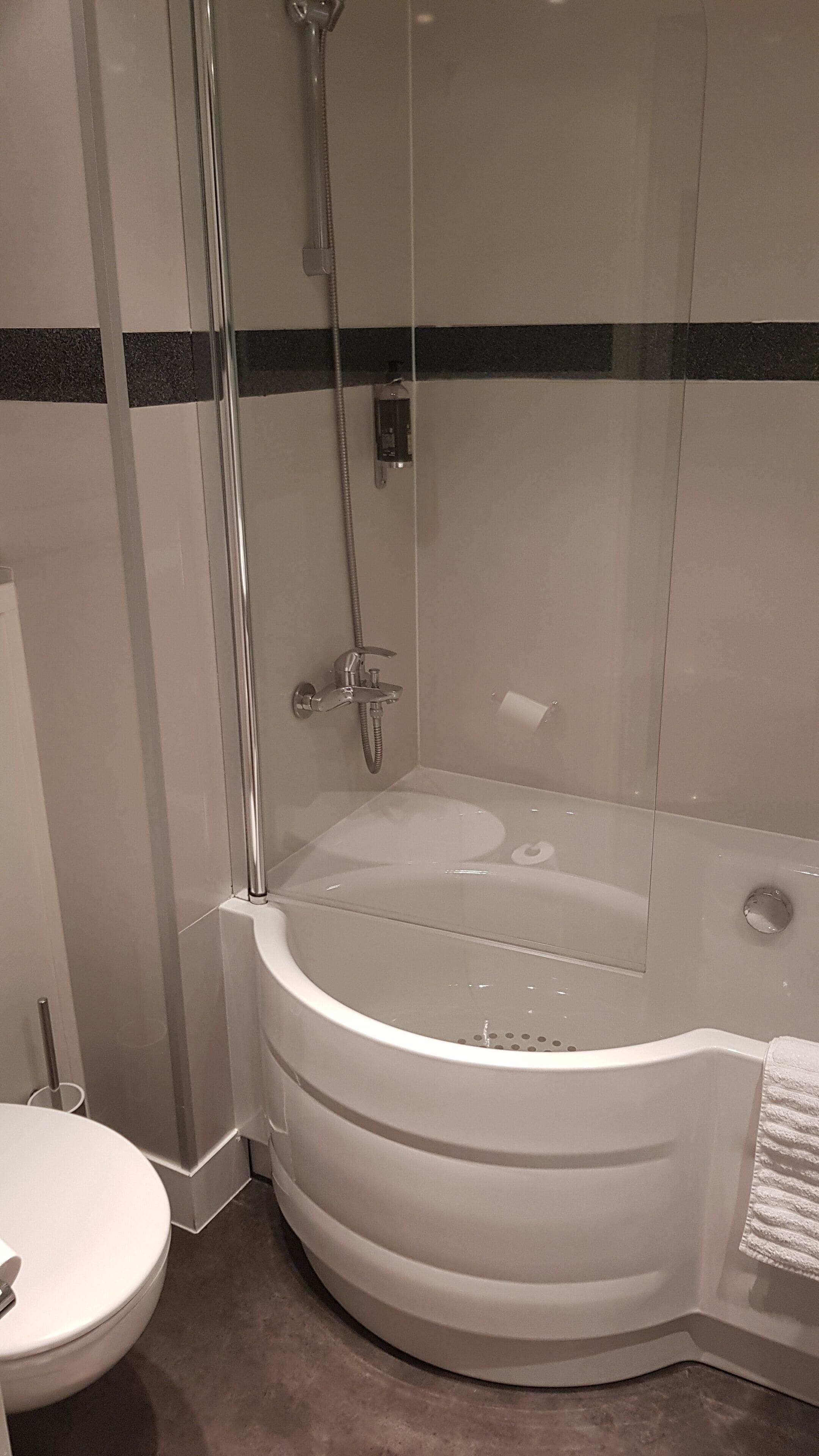 A modern bathroom with a glass-enclosed shower, a white bathtub, and a toilet.