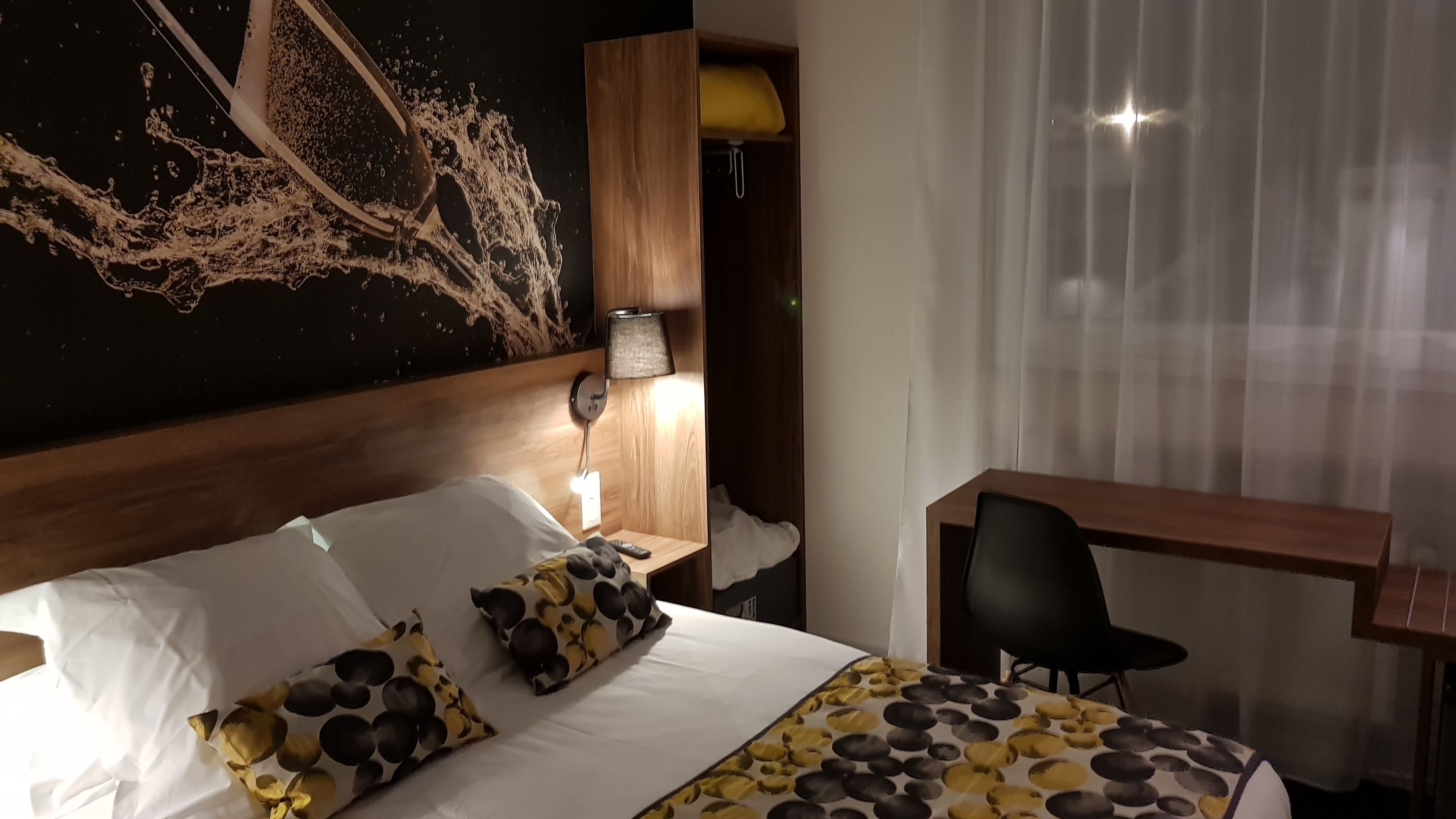 Une chambre d’hôtel comprenant un lit, un bureau, une chaise, une lampe et un mur au décor texturé.