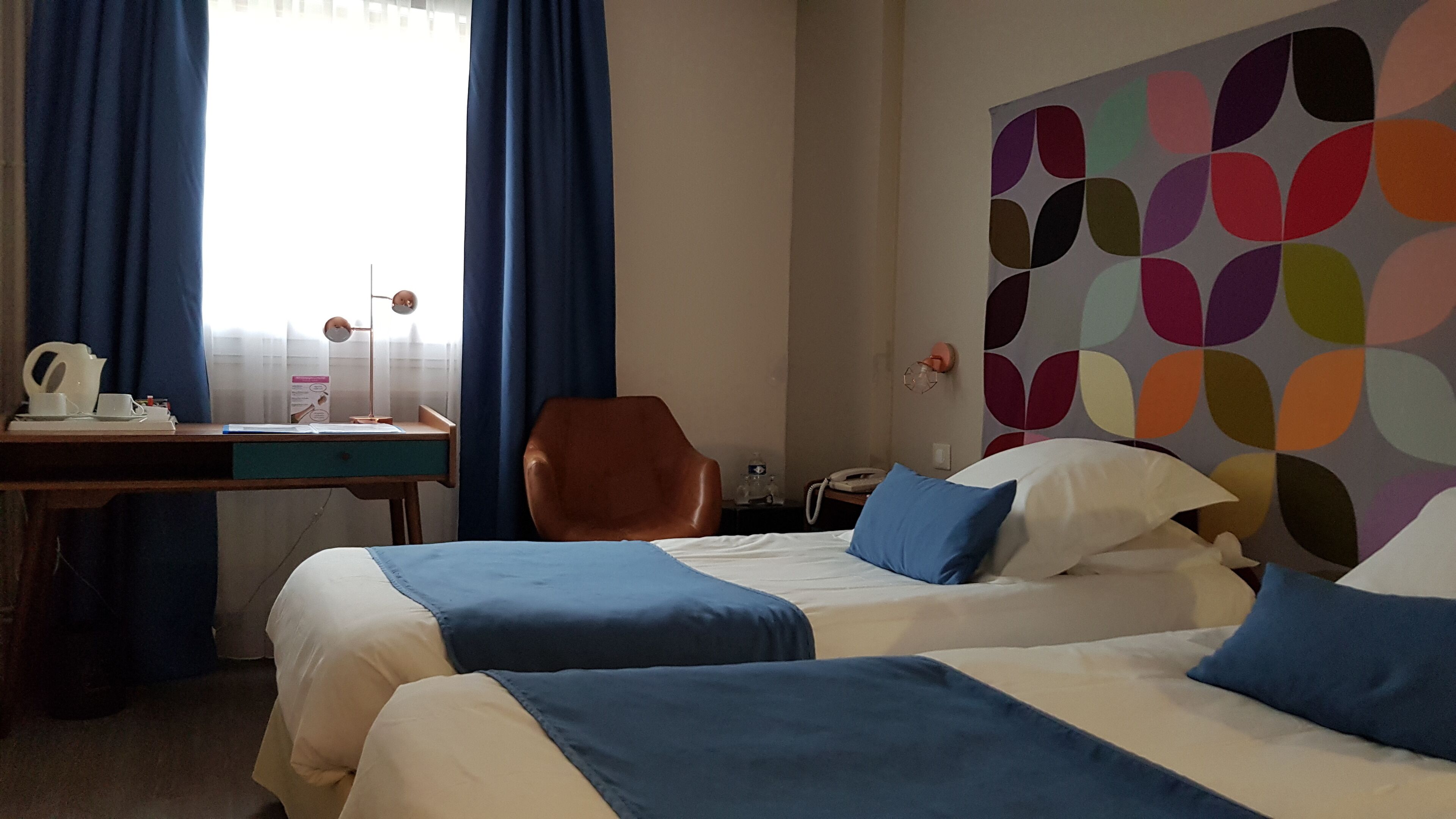 Habitació d'hotel amb dos llits, un escriptori, una cadira, un telèfon i una paret de colors.