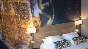 A hotel room with a bed, white bedding, a headboard, two bedside lamps, a nightstand, and a wall mural. - Hôtel de Champagne (Epernay)
