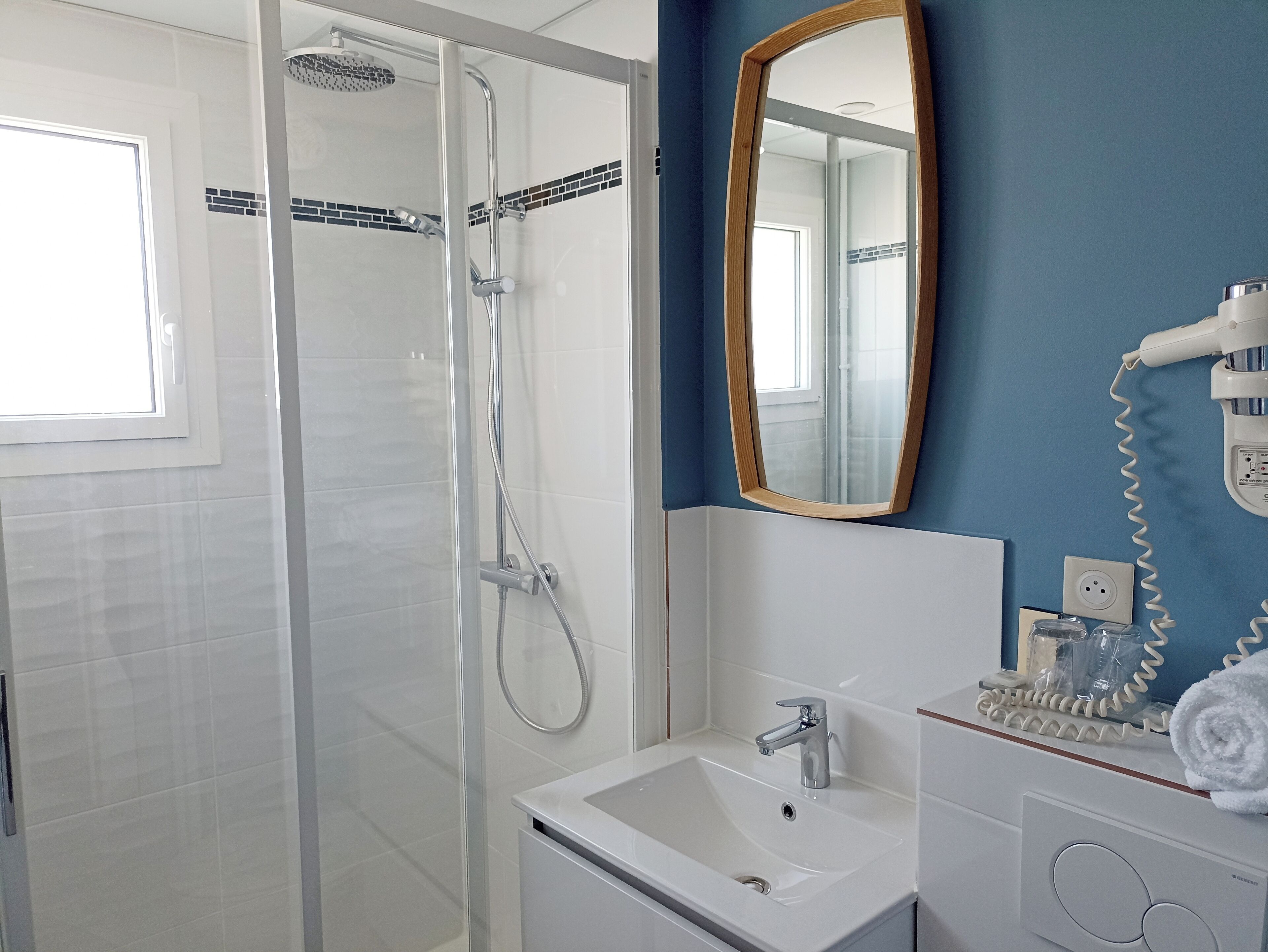 A bathroom with a glass-enclosed shower, a white sink, and a mirror with a wooden frame.