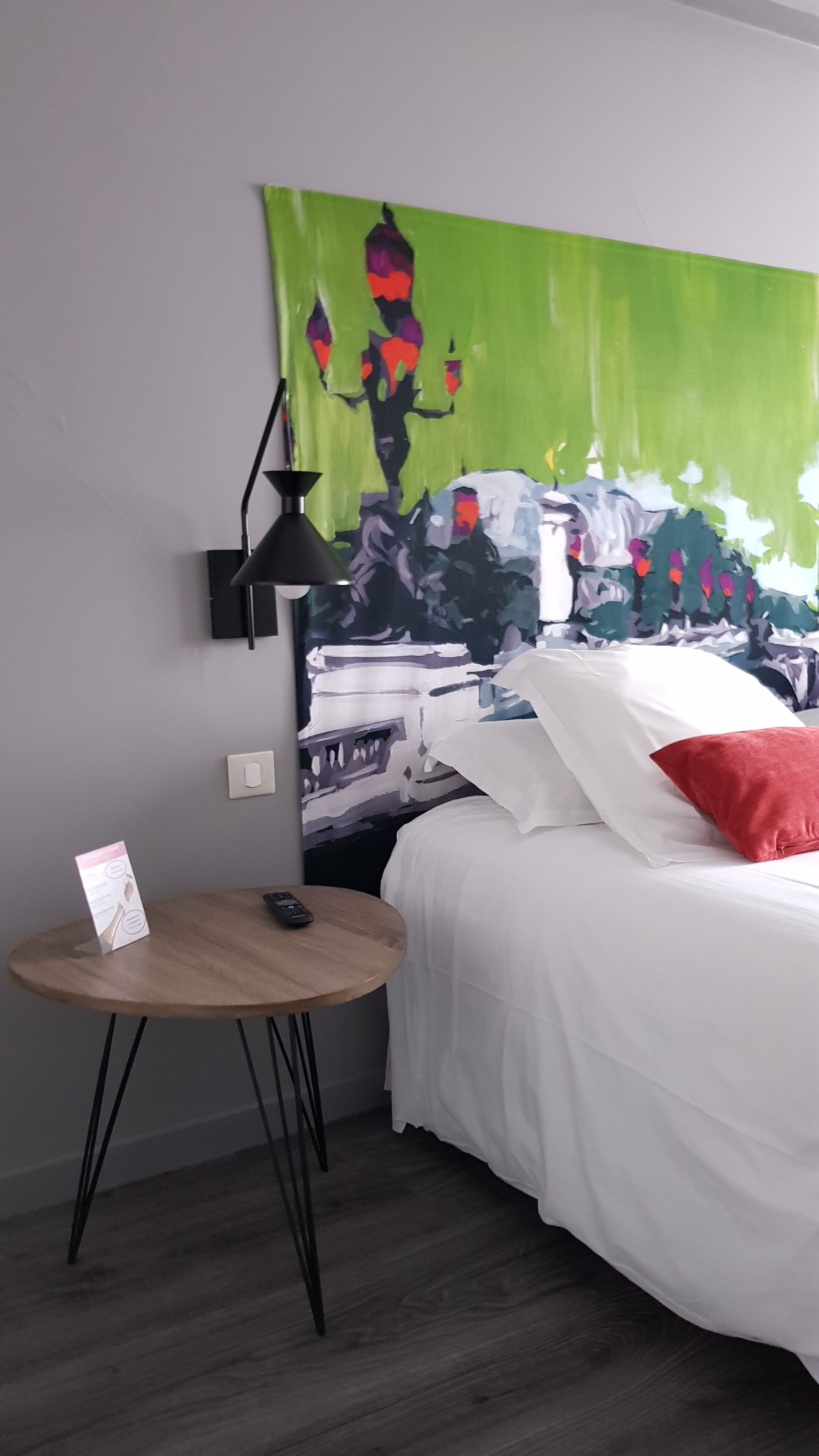 A bedroom with a bed, a small round table, a lamp, and a painting on the wall.