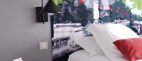 A bedroom with a bed, a small round table, a lamp, and a painting on the wall.