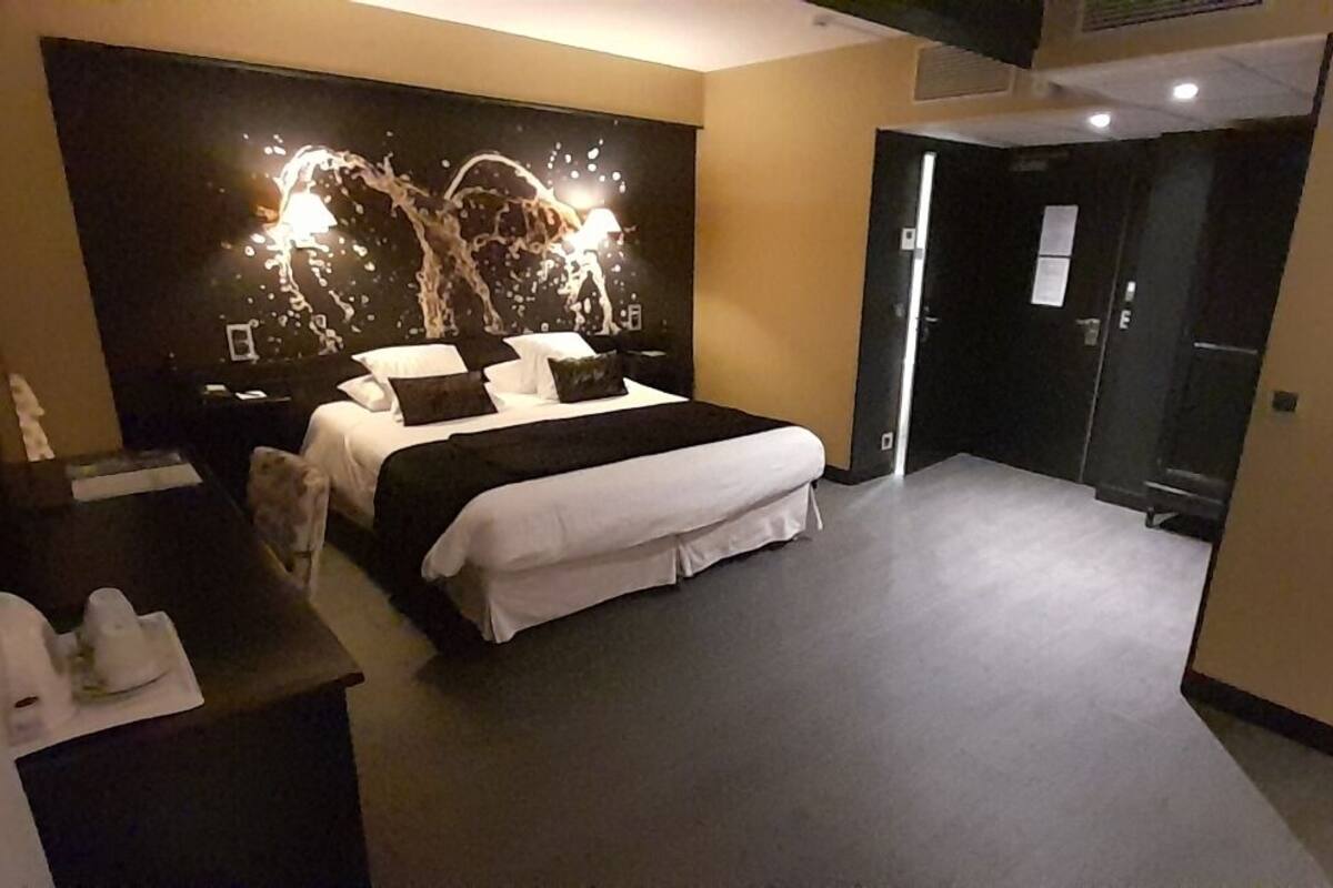 A modern hotel room with a large bed, a headboard with a unique design, bedside tables, and a wardrobe.
