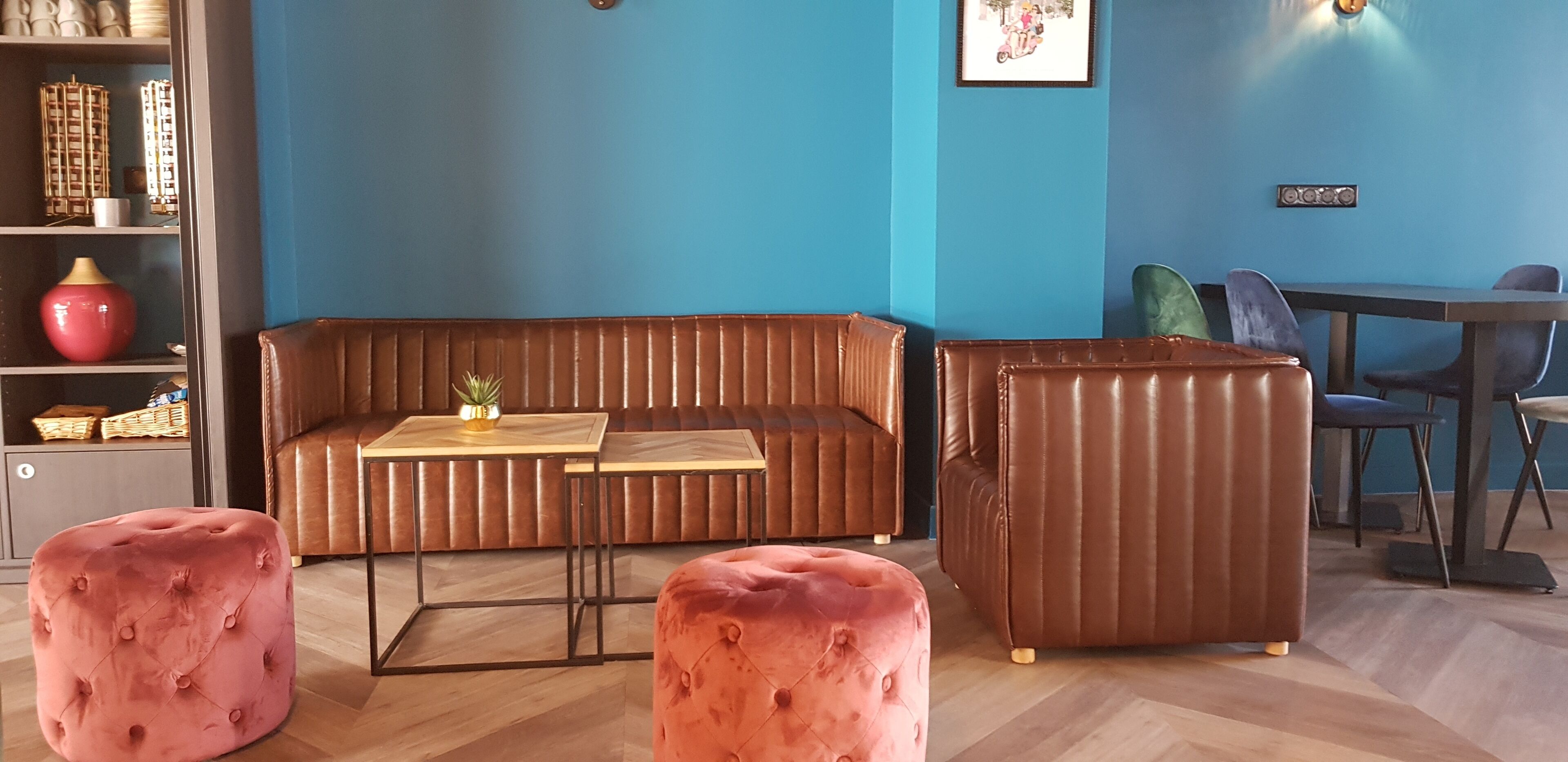 A modern living room with a blue wall, a brown sofa, a small table, and two pink ottomans.