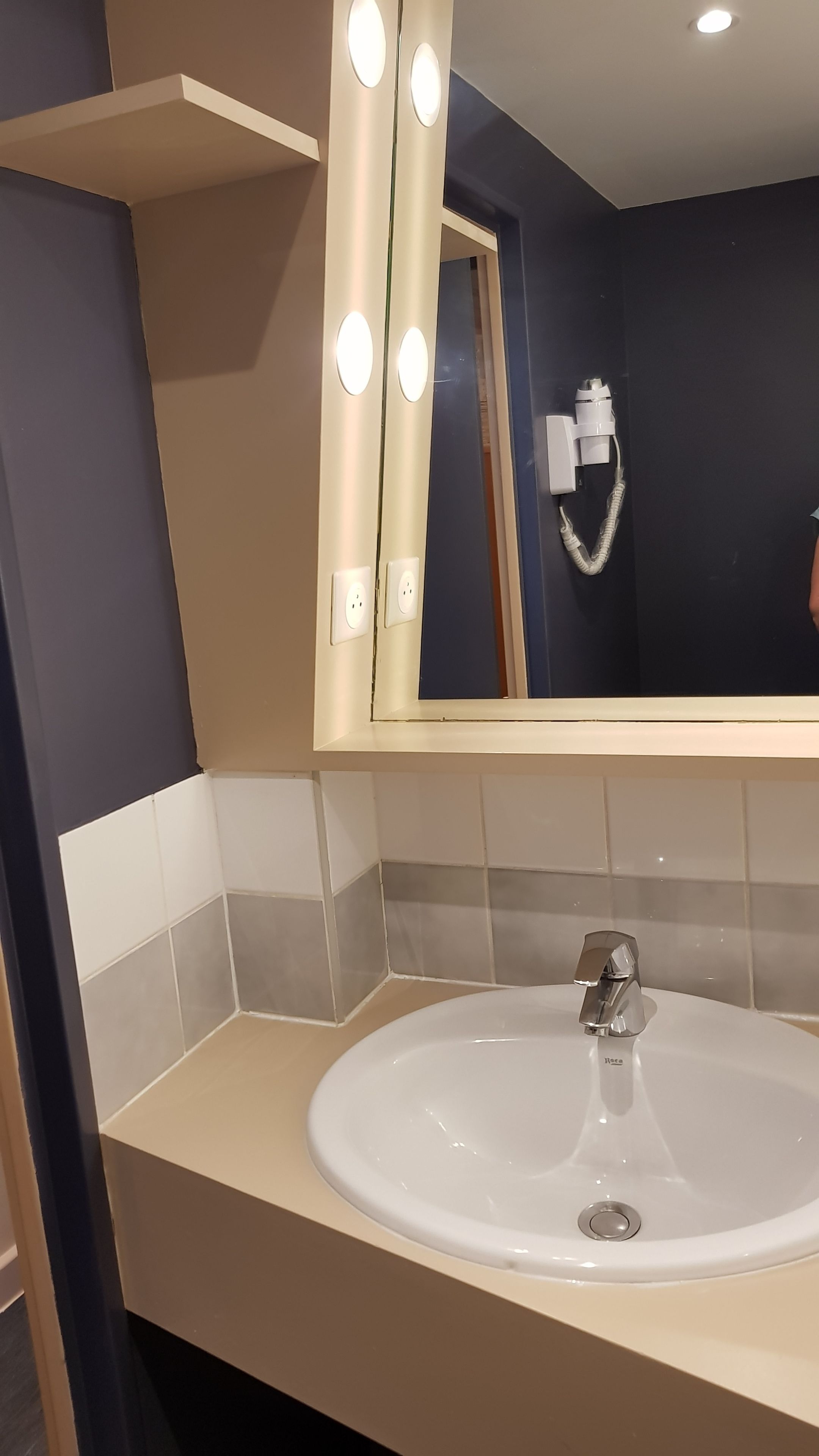 Een badkamer met een witte wastafel, een spiegel met verlichting en een handdoekhouder.