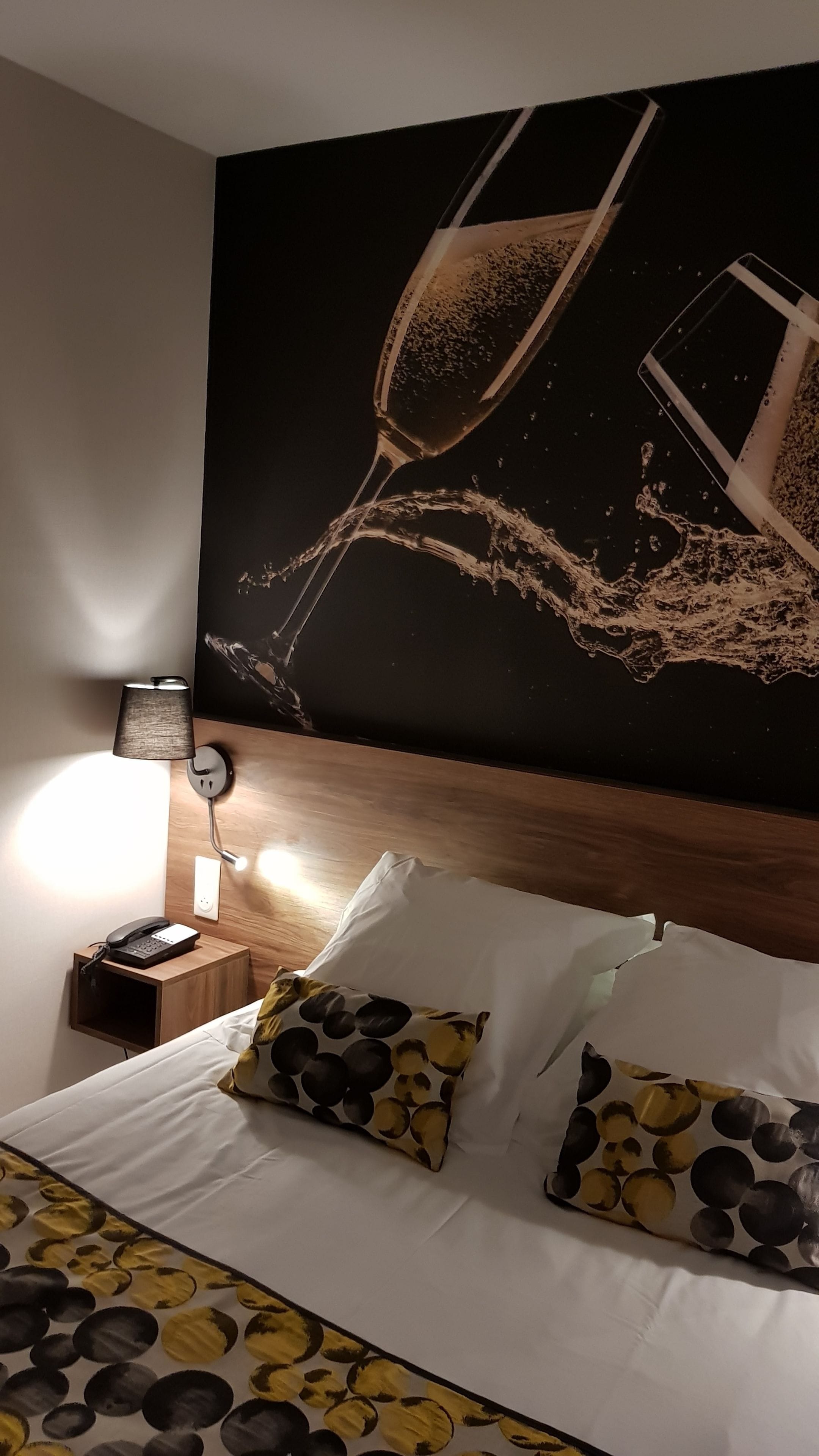 Habitación de hotel con cama, mesita de noche con lámpara y un cuadro abstracto grande en la pared.