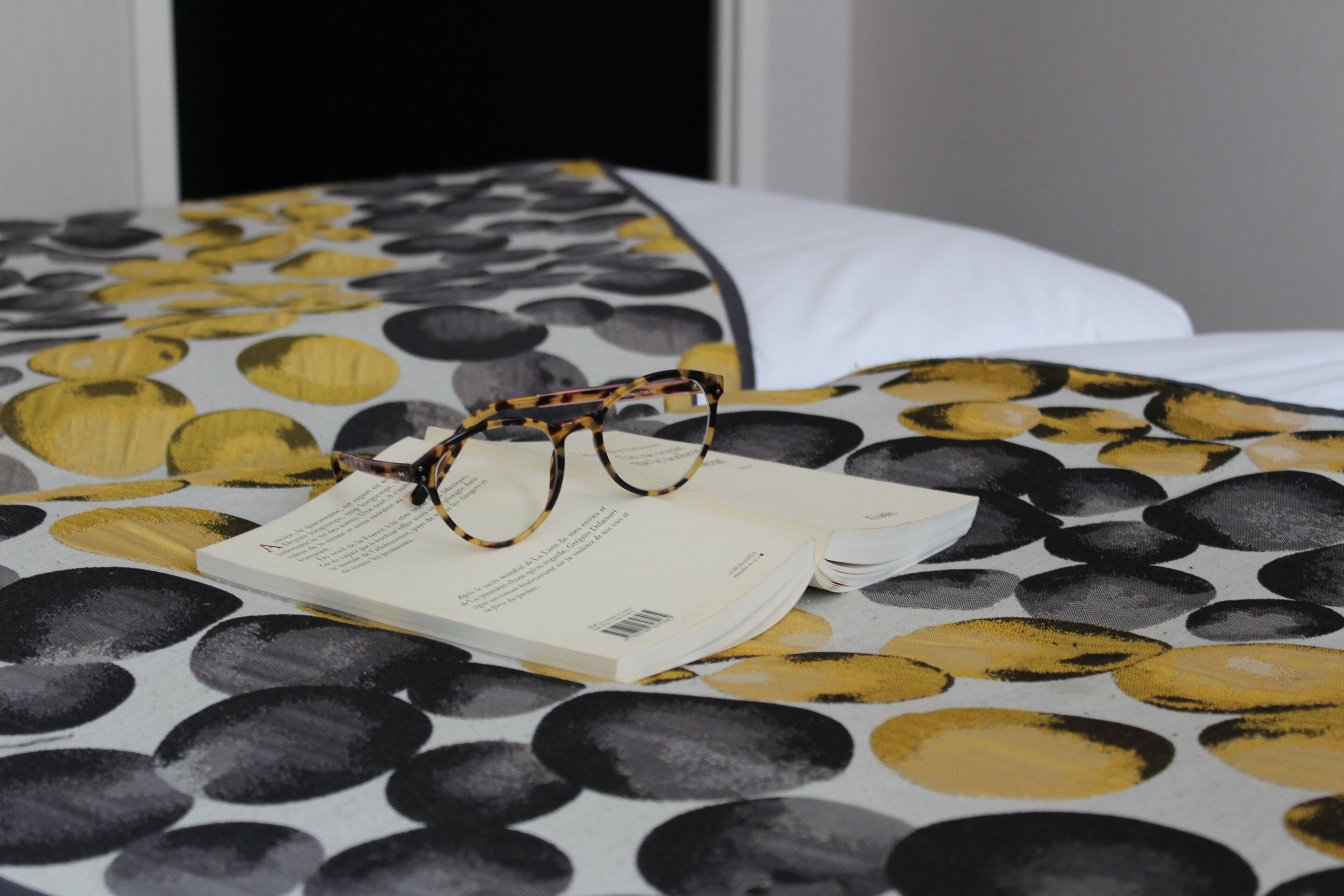 A bed with a patterned bedspread, a book, and a pair of glasses on it.
