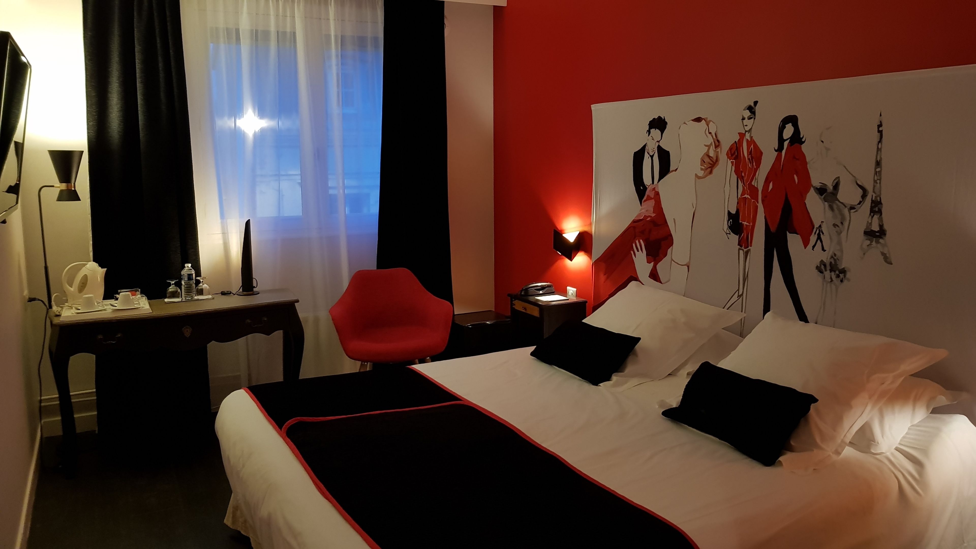 Ein Hotelzimmer mit Bett, Schreibtisch, Stuhl, Lampe und einem Wandbild.