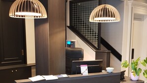 A reception desk with two pendant lights, a digital screen, and a plant. - Hôtel de Champagne (Epernay)