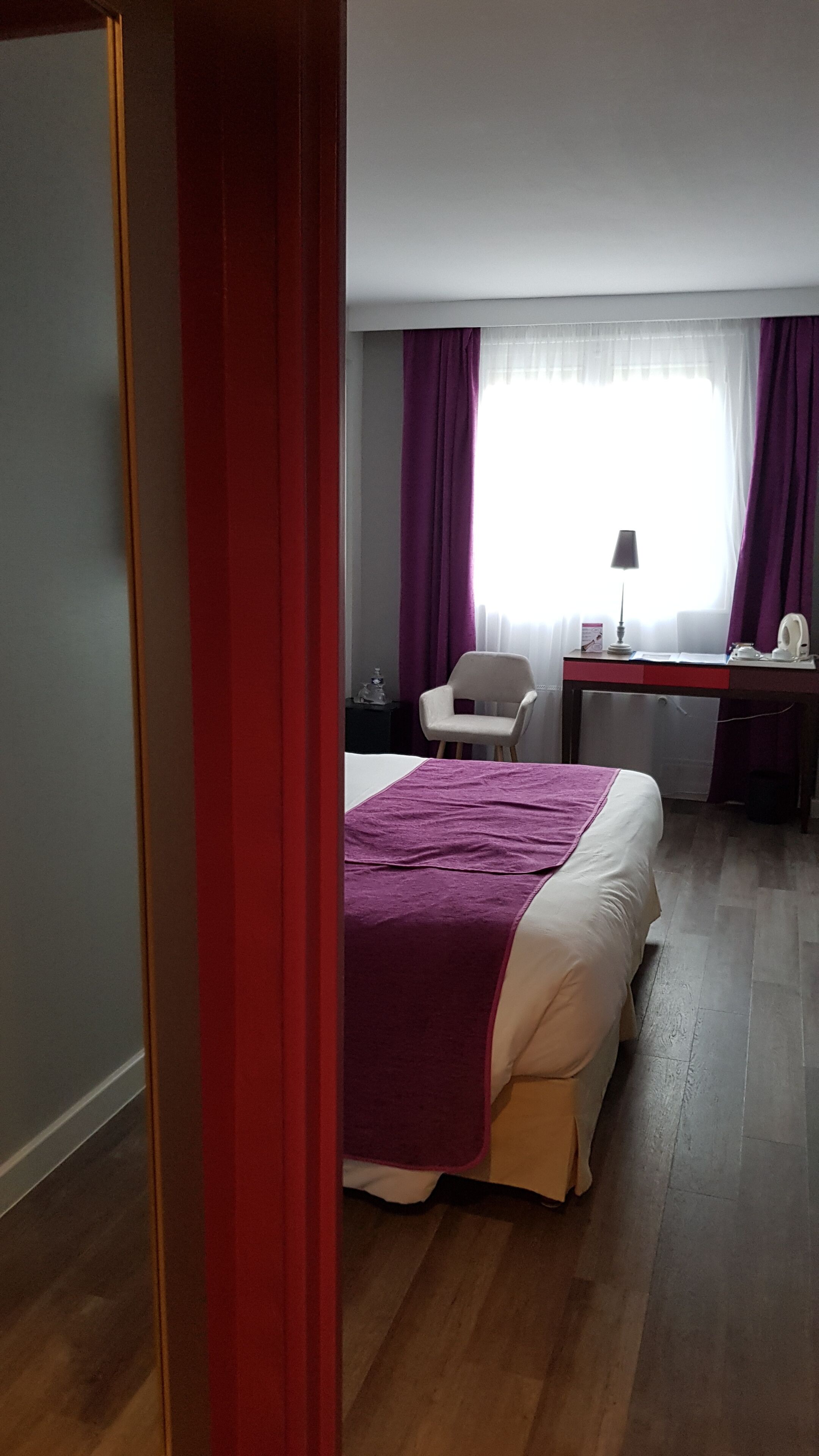 Een hotelkamer met een bed, een bureau, een stoel en een raam met gordijnen.