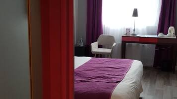 Een hotelkamer met een bed, een bureau, een stoel en een raam met gordijnen.