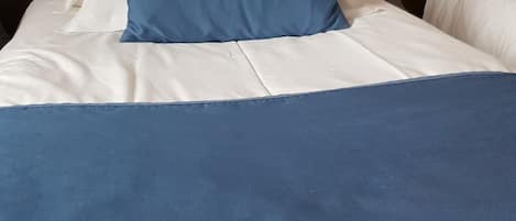 A bed with white and blue bedding, a blue pillow, and a colorful abstract wall design.