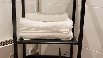A black metal shelf unit with white towels, a tissue box, and a glass vase with a plant.