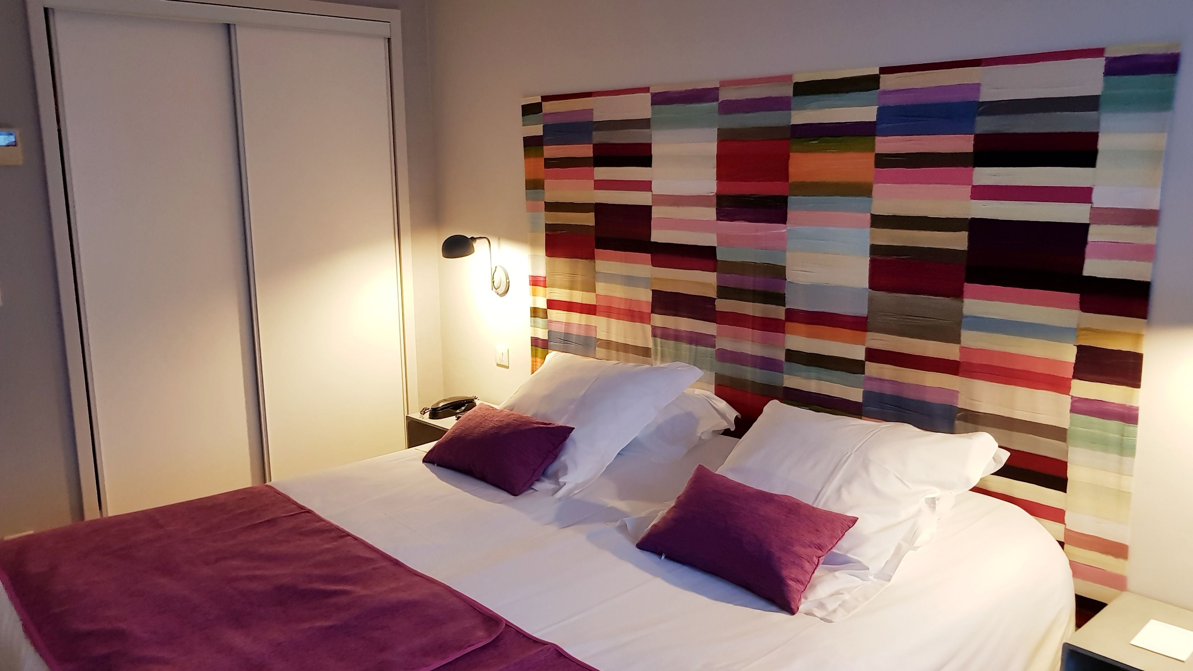Een hotelkamer met een bed, een nachtkastje, een telefoon en een wand met een kleurrijke quilt.