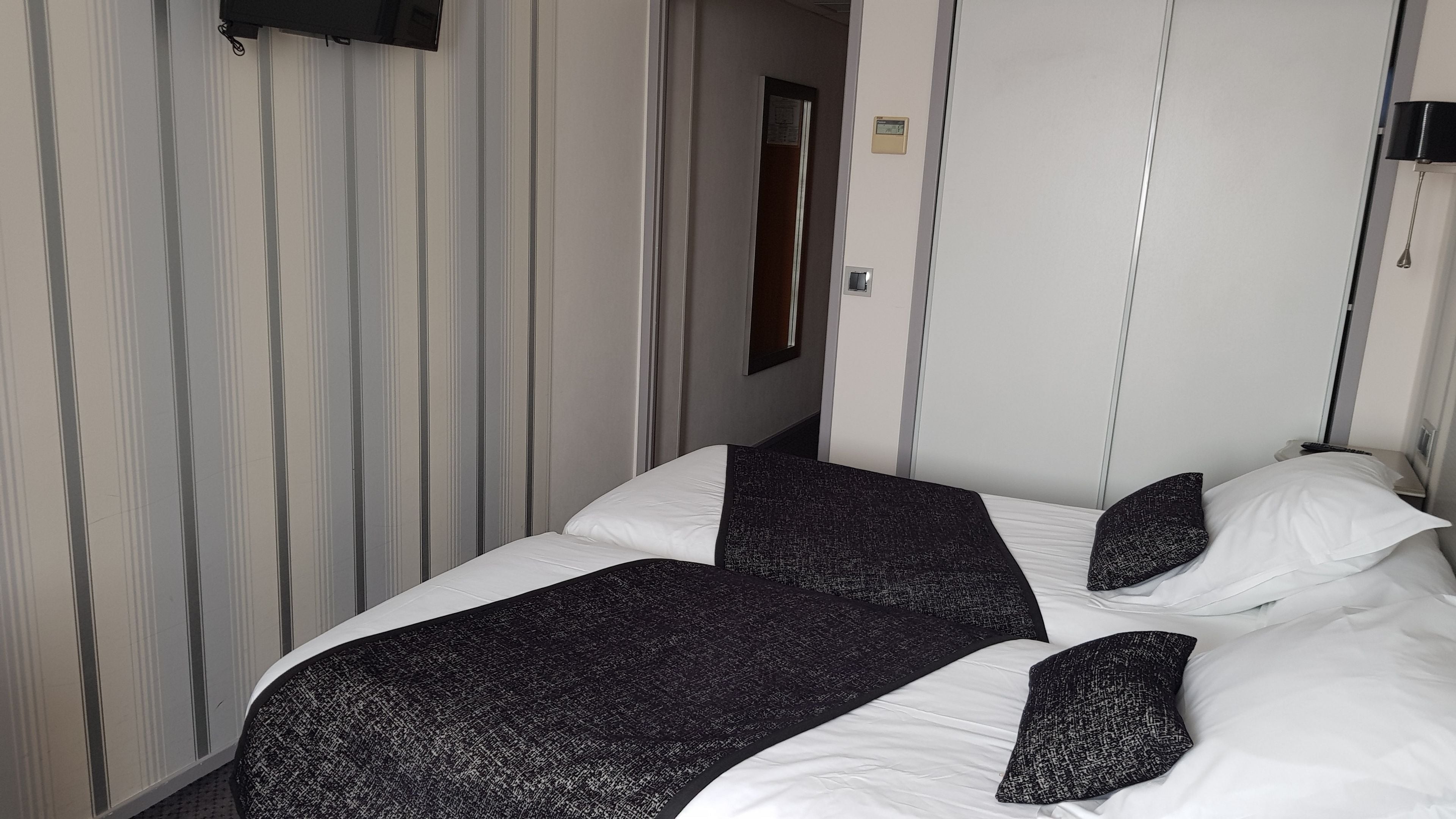 Una habitación de hotel con una cama, un televisor montado en la pared y una puerta que da a otra habitación.