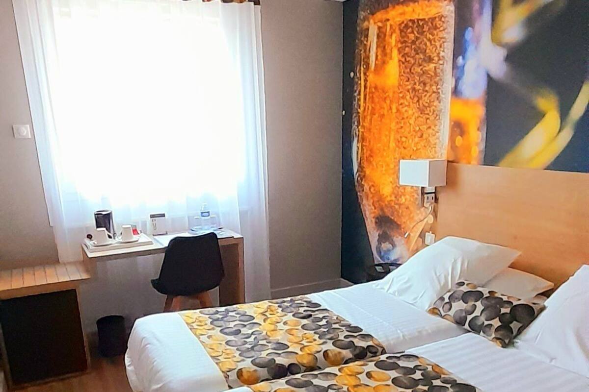 A hotel room with two beds, a desk, and a large window with curtains.