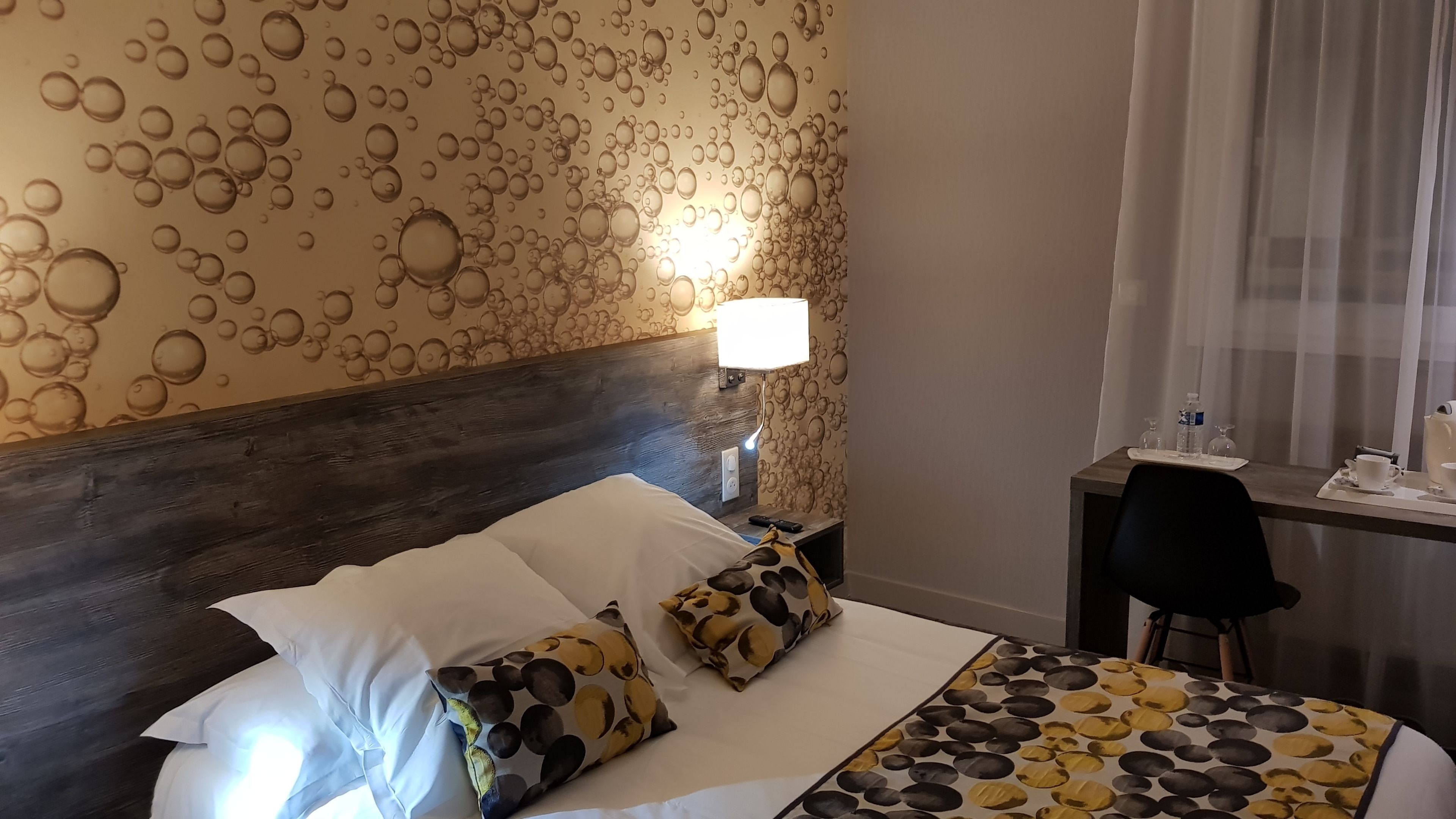 A hotel room with a bed, a nightstand, a desk, and a lamp.