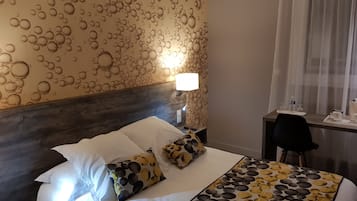 A hotel room with a bed, a nightstand, a desk, and a lamp.