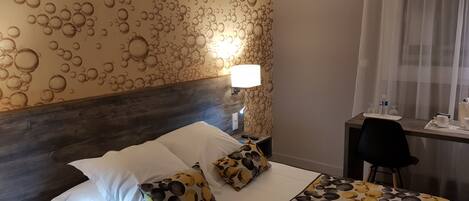 A hotel room with a bed, a nightstand, a desk, and a lamp.