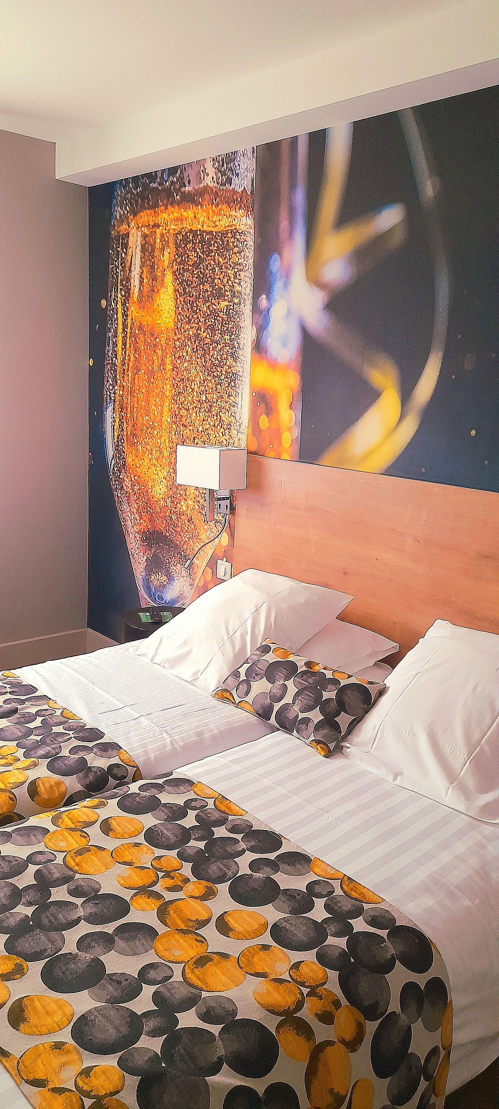 A hotel room with a bed, pillows, and a large abstract painting on the wall.