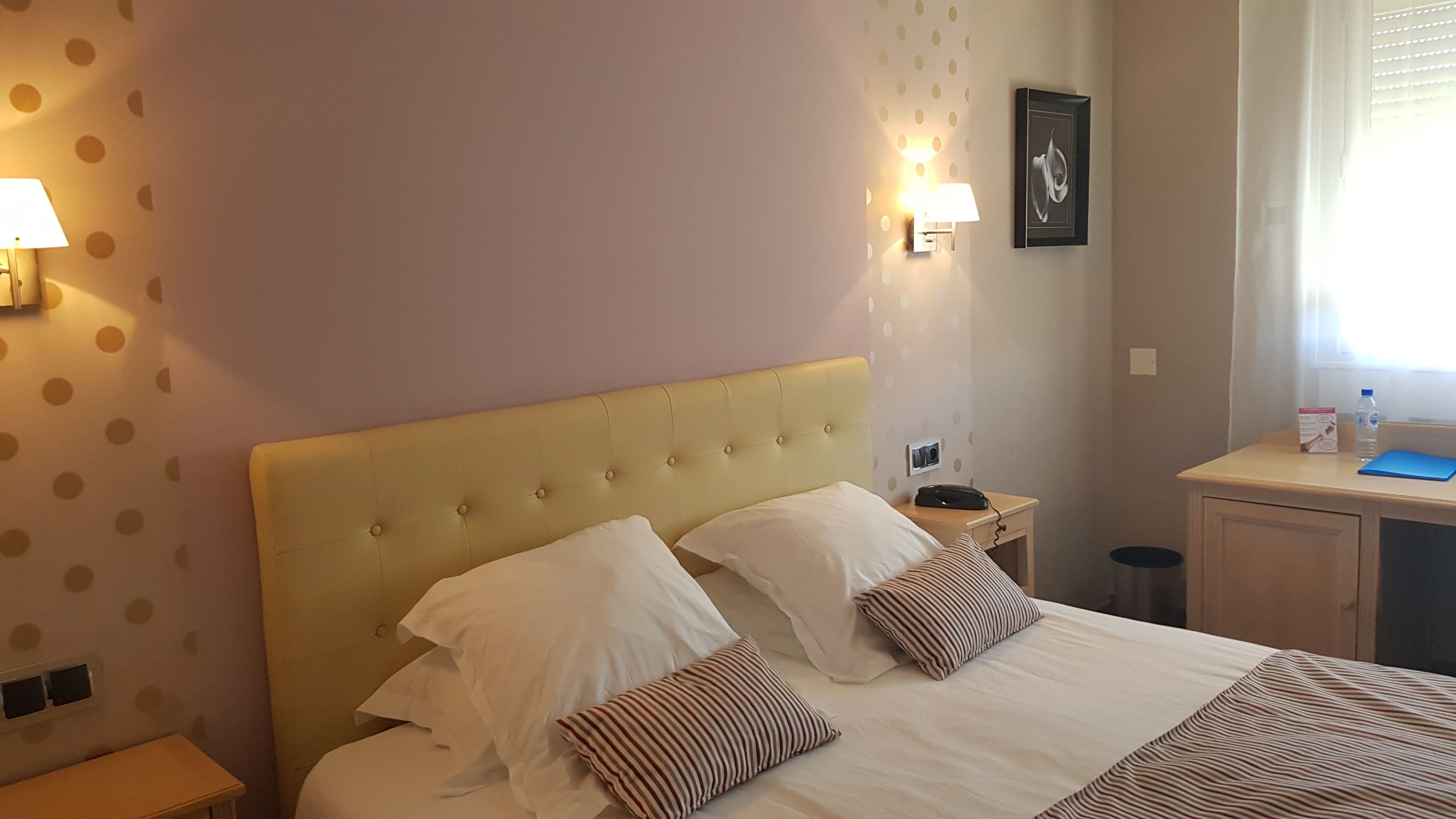 Een hotelkamer met een bed, twee bedlampen, een nachtkastje, een bureau en een raam met jaloezieën.