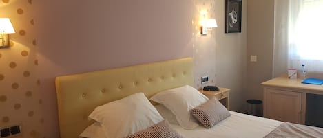 Habitación de hotel con cama, dos lámparas de noche, una mesita de noche, un escritorio y una ventana con persianas.