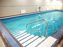 Una piscina con una escalera metálica y escalones de cerámica que dan al agua.