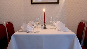 A dining table set with white tablecloth, candles, and wine glasses, with a framed picture of a dog on the wall above. - Parkhotel (Nieheim)