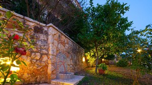 Un muro de piedra con una pequeña fuente, rodeado de follaje y plantas en macetas.