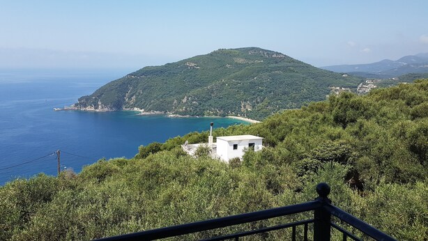 Paisaje costero con una colina, un edificio blanco pequeño y un mar azul claro.