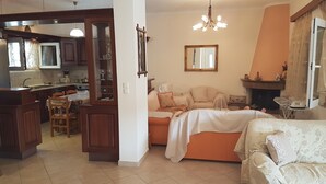 Un salón amplio con sofá, una mesa de comedor con sillas, una cocina con armarios y una ventana, y una chimenea.