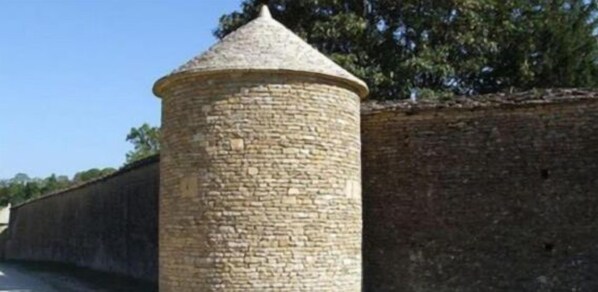 Una torre de piedra con techo cónico, parte de un muro de piedra más grande.