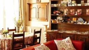 A dining area with a table set for two, a red sofa, and a bookshelf filled with books and decorative items. - Le Puits Fortifie (Salives)