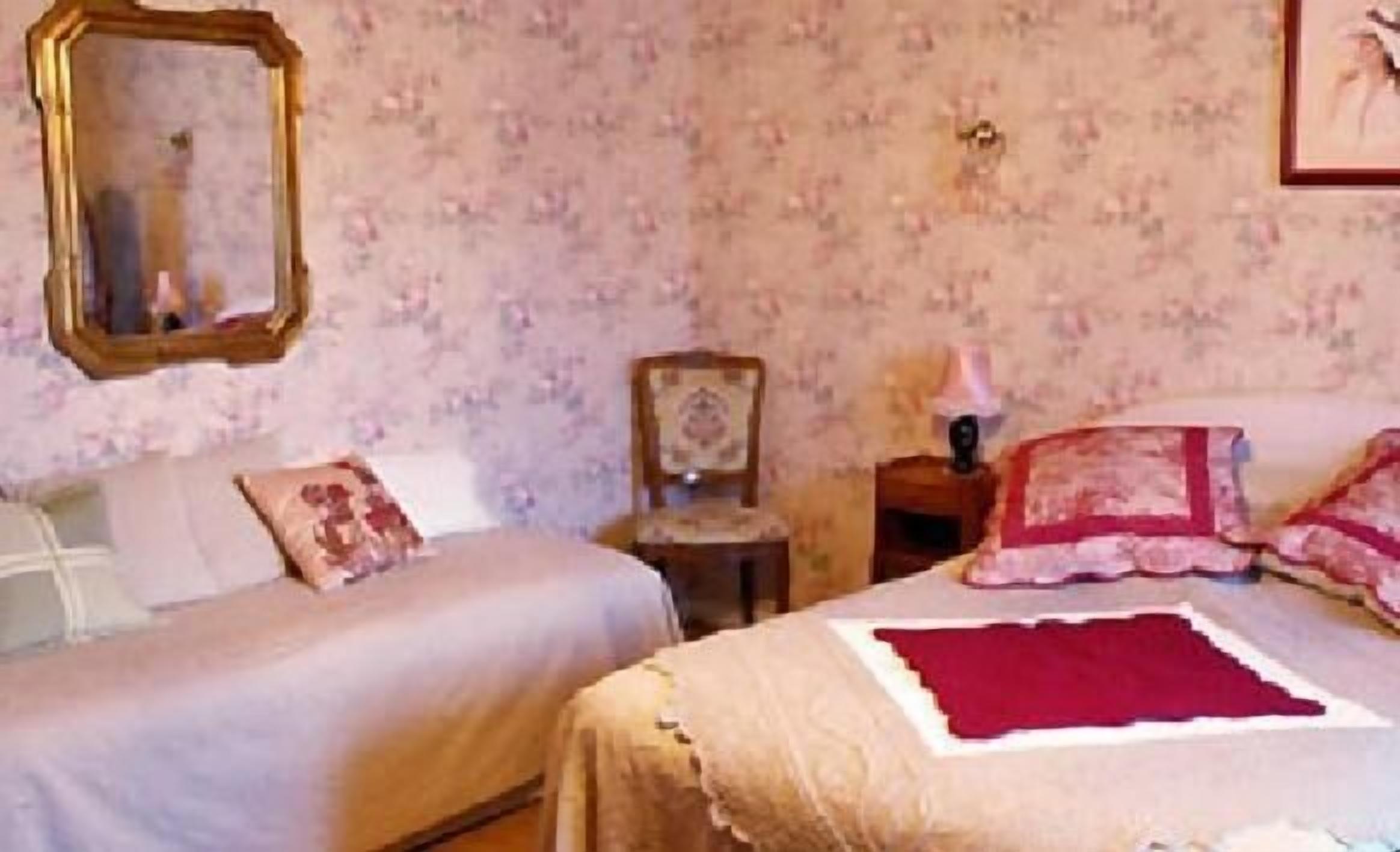 Une chambre avec deux lits, un papier peint à motifs floraux, un miroir et une table de chevet avec une lampe.