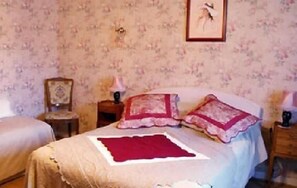 A bedroom with floral wallpaper, a bed with two pillows, a nightstand with a lamp, and a framed picture on the wall. - Le Puits Fortifie (Salives)