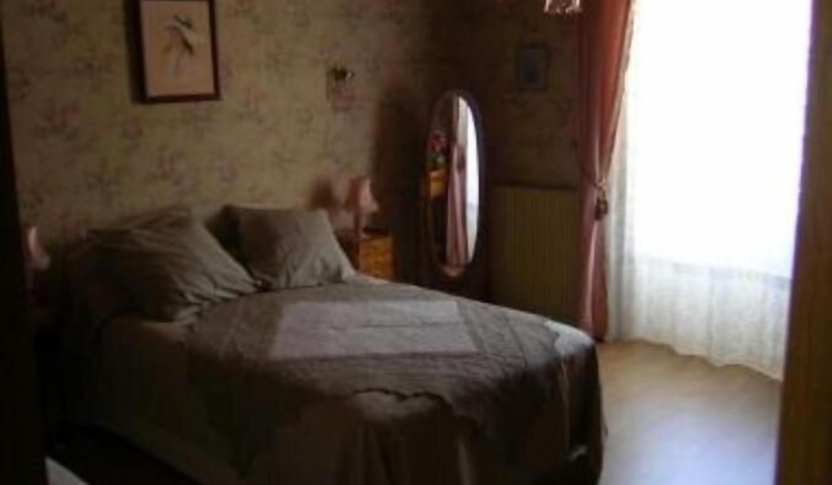 Une chambre à coucher avec un lit, un miroir et une fenêtre avec des rideaux.