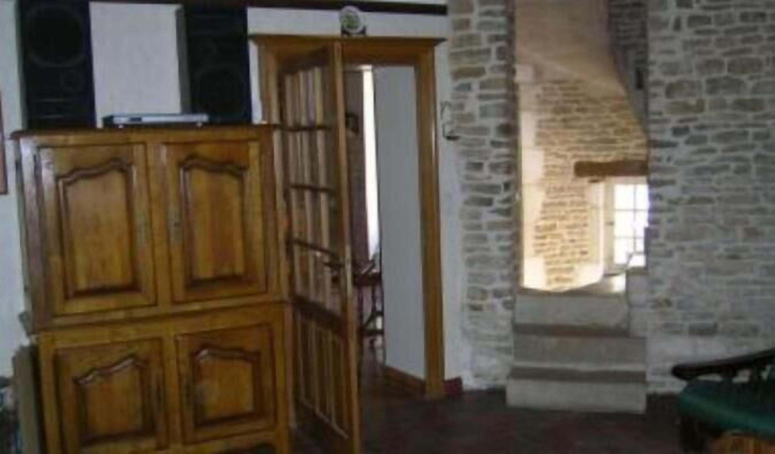 A room with a wooden cabinet, a stone wall, and a doorway leading to another room.