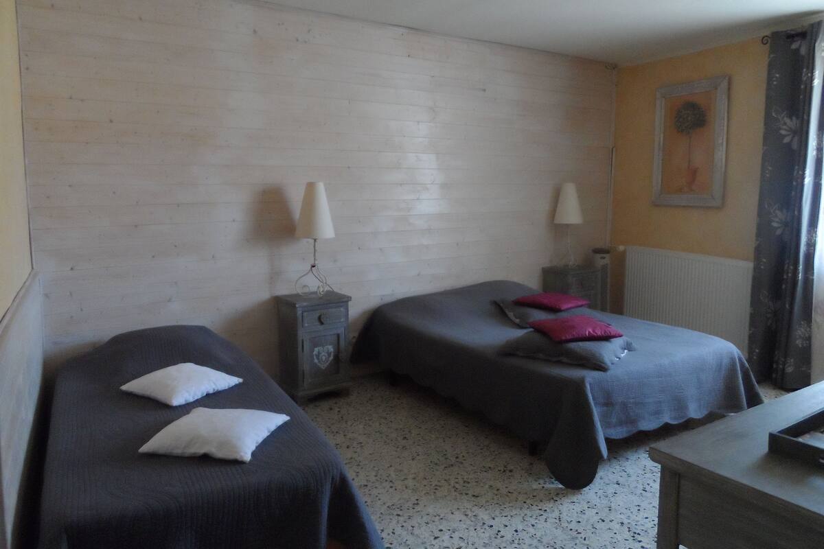 A room with two single beds, each with a pillow and a bedside table with a lamp.