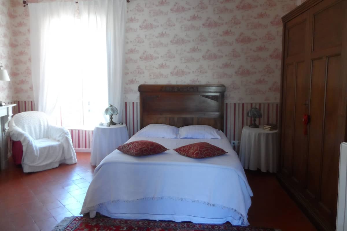 A bedroom with a bed, a chair, a lamp, and a wardrobe.